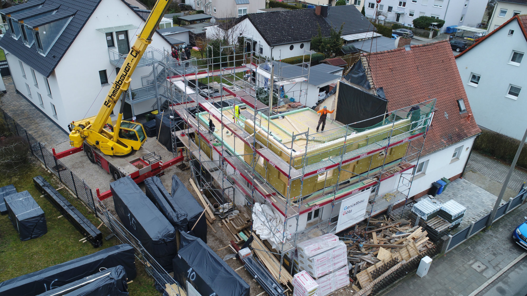 Cantiere residenziale con edificio in ristrutturazione, impalcature, pannelli isolanti gialli e gru Schmidbauer.